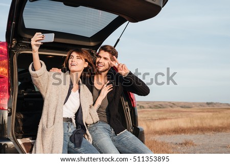 Portrait of a happy smiling couple taking selfie with mobile phone while sitting inside car outdoors