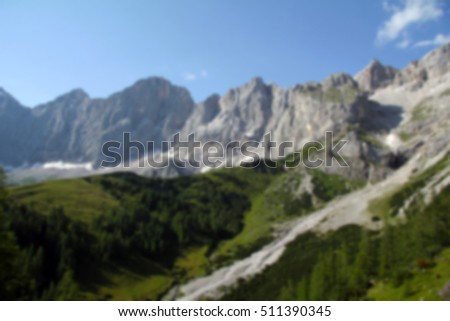 Blurred background. Landscape: the mountains covered with snow on top and green grass at the bottom of the foot. Dachstein, Alps, Austria. Landmark.
