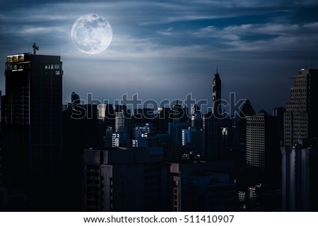Silhouettes of skyscrapers different construction in the dark town with background of a large moon and clouds at nighttime. Dark tone and high contrast style. The moon were NOT furnished by NASA. Royalty-Free Stock Photo #511410907