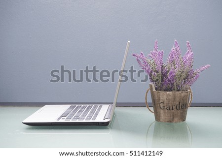 Office table with violet flower on pot and laptop.