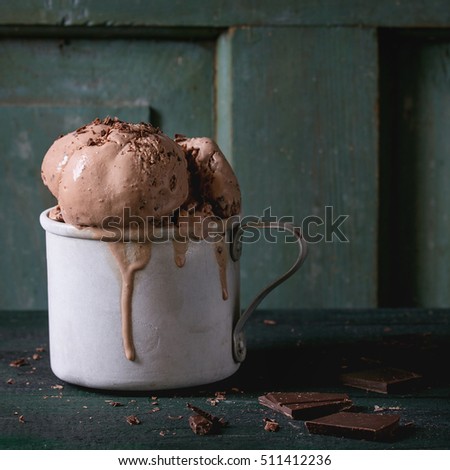 Frozen vintage aluminum mug with melting chocolate ice cream balls, served with chopped dark chocolate on old wooden table. Dark rustic style. Space for text. Square image