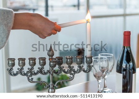 Hanukkah - Jewish holiday of light with menorah and bottle of red wine with two glasses by the window