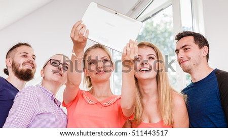 Fun bonding selfie concept. Group of diverse friends students classmates taking self photo with tablet pc computer indoors in class