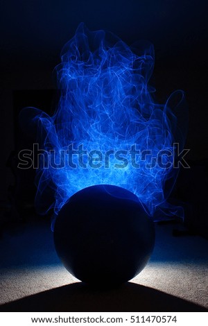 An Orb in Silhouette with Blue Flames Shooting from the Top - with a Bright Light and Long Shadow on the Ground 