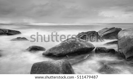 Sea waves crashing over rocks on the  stone beach in rain time and created by the agitation of seawater in the moment of ocean waves crashing against rocks; Black and White picture