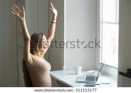 Portrait of a young attractive cheerful woman, celebrating success, victory, sitting at the laptop. Small home office interior. Business concept photo, lifestyle