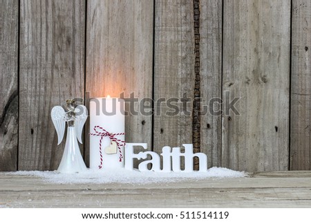 White holiday candle with candy cane striped bow and heart, angel, and the word Faith  in snow by antique rustic wood background; Christmas and religious background 