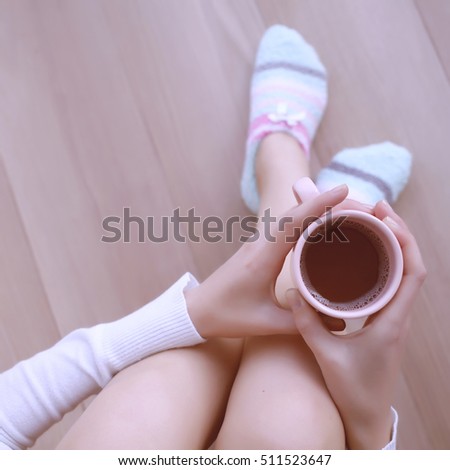 Comfort Concept - Woman drinking hot cocoa and sitting on the floor parquet. Close-up of female legs in bright colored warm socks with a retro vintage instagram filter, top view