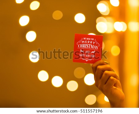 Hand holding Merry Christmas and Happy New Year greeting card on bokeh background, festive defocused lights.
