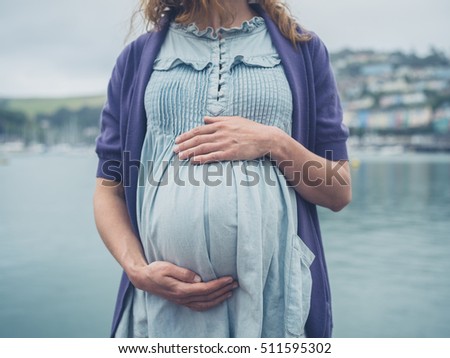 A young pregnant woman is standing by the river in a small seaside town