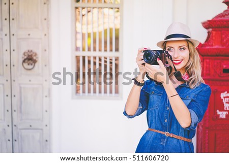 Hobby and fashion. Young pretty woman in hat holding camera on old town street.