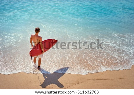 It's time for surfing! Young man holding surf board on the sea shore.