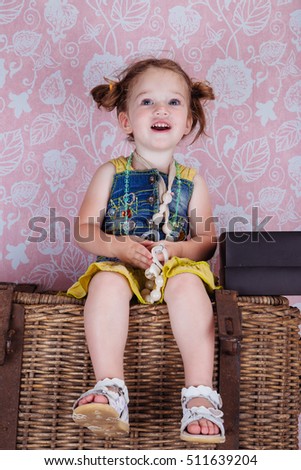little cute girl sitting on a wicker basket and laughs, photo shoot in the studio