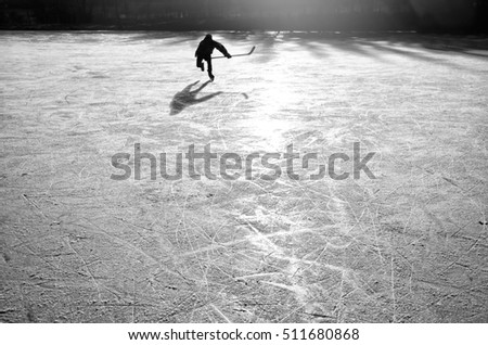 Young hockey player on the natural ice during calm winter sunset. Sport active winter wallpaper with space for your montage.  - black and white photo.
