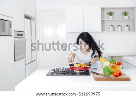 Picture of a pretty Asian woman cooking in the kitchen and sniff meal on the frying pan, shot at home