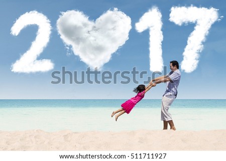 Picture of happy little girl and her father playing together on the beach with number 2017 on the sky