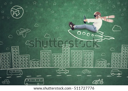 Image of little kid riding rocket picture and doodles on the chalkboard while imagining fly in the city