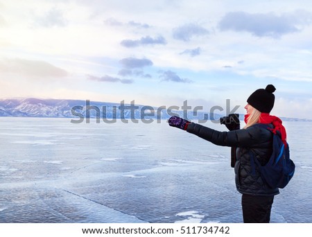 Woman tourist photographer is indicating something outside standing at frozen surface of lake Baikal. Winter tourism concept.