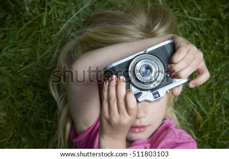 Portrait of little girl taking picture using vintage old retro film camera, lying on grass background