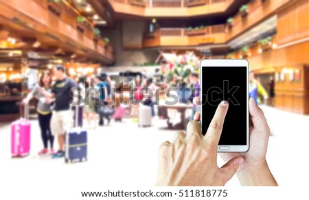 Man use mobile phone, blur image of guests and luggage in lobby as background.