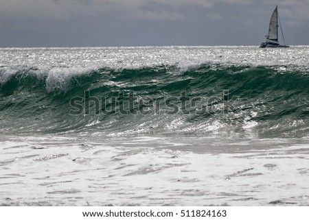 breaking wave with sailboat in background, cloudy sky