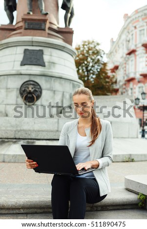 the girl has sat down to work behind the laptop. On the street excellent weather. The girl smiles very hard works.