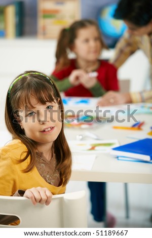 Elementary age child sitting at desk looking at camera in art class in primary school classroom.