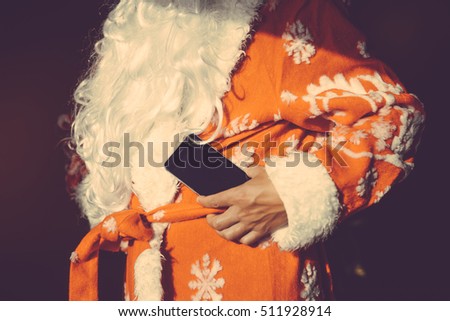 Santa Claus holding in hands mobile phones ready for Christmas time. Social activity during festive period. Red white light background