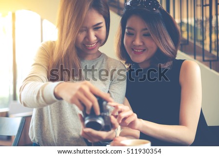 Happy charming women are checking and looking at their picture on the camera LCD display screen with a big smile after shooting in the coffee shop cafe. Feeling funny and happiness.