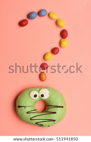 Green funny surprised glazed donut with chocolate and colorful dragee with raisins or peanuts inside on pink background
