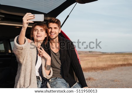Beautiful excited couple making selfie while sitting inside car at the seaside