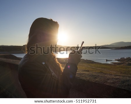 Beautiful young woman taking pictures. Silhouette of a woman. Taking photos of a lake during sunset.