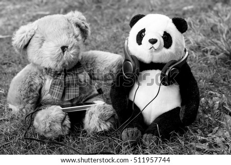 stuffed panda and Teddy Bear wearing headphones in the green lawn .Sharing the joy of life concept.black and white picture