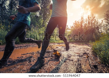 Two trail running athletes crossing the dirty puddle Royalty-Free Stock Photo #511964047