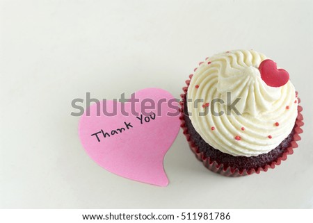 Cupcake with red heart and pink sticky note with handwriting words thank you with copy space on off white table