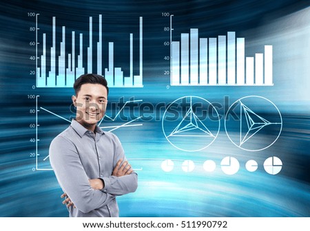 Smiling Asian man in blue shirt is standing in blue room with four graphs in the air. Concept of futuristic tomorrow.