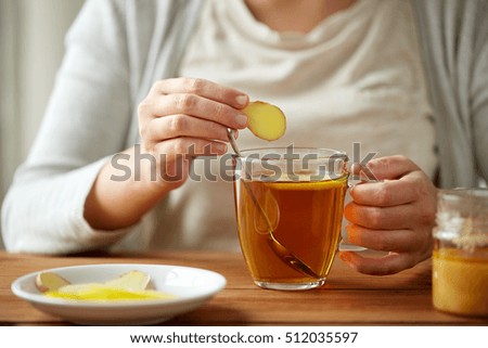 health, traditional medicine and ethnoscience concept - close up of woman adding ginger to tea cup with lemon and honey Royalty-Free Stock Photo #512035597
