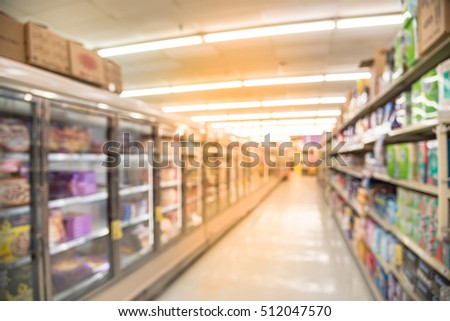 Blurred image of frozen foods with ice cream, frozen pizza, desert and baby food, baby wipes, diapers aisle in store. Wide view supermarket shelves variety of product, defocused background bokeh light