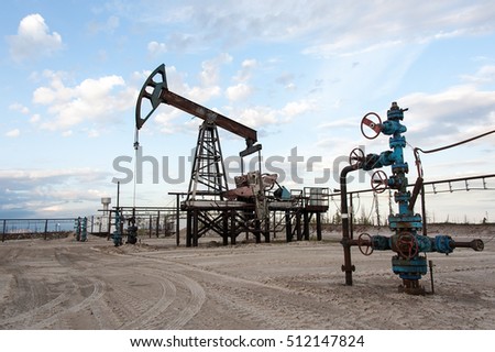 Oil pump jack and wellhead with valve armature during sunset on the oilfield. Extraction of oil. Oil and gas concept. 