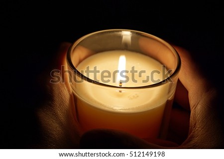 Male hands holding a candle in the transparent glass shining in the darkness as a symbol of contemplation, meditation and calmness