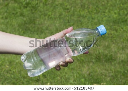 Plastic bottle with water in female hands on a background of green grass
