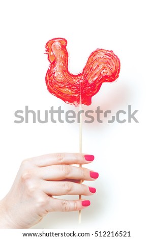 symbol 2017. Sweet lollipop red rooster holding a woman's hand with nail polish on a white background
