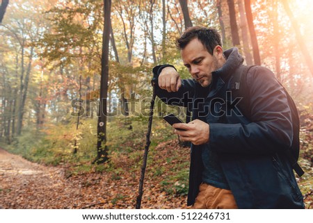 Man hiking in autumn colorful forest and using phone