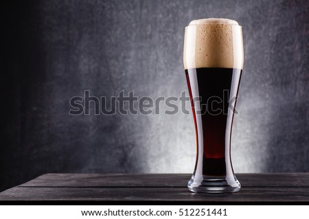 Tall glass of dark beer over a dark textured wooden background Royalty-Free Stock Photo #512251441