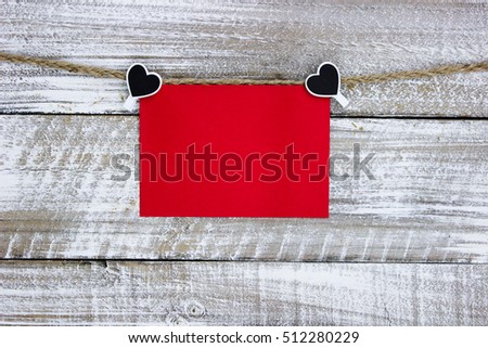 Red note card or blank sign hanging on clothesline with hearts and whitewash rustic antique wood background; Valentine's Day, Christmas and love concept with white painted copy space