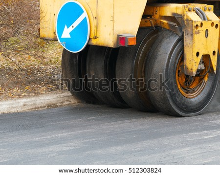 Road construction works with tyred road roller finishes asphalt with road sign on it, steam goes from fresh asphalt