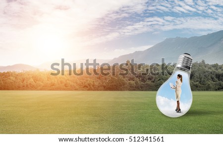 Young businesswoman trapped inside of light bulb on green grass