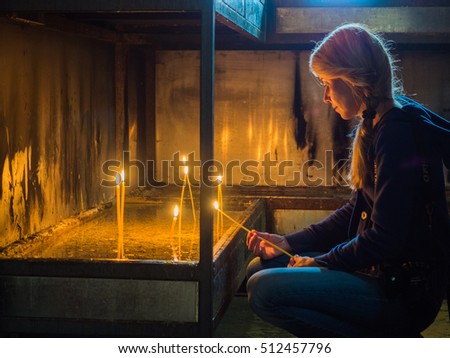 Picture of the girl with long fair hair lighting wax candles in a church. Female discovers spiritual order in a church. The girl looking to the wax candle's flame.