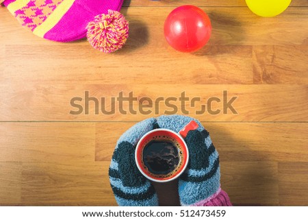 Top view women's hands, gloves, Silk hat, colored balls and a cup of coffee on wood table. In the winter. Warm up with hot coffee, sunlight helps the body to warm up.