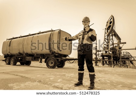 Worker talking on the radio near pump jack and tank trailer in the oilfield. Oil and gas concept. Toned.